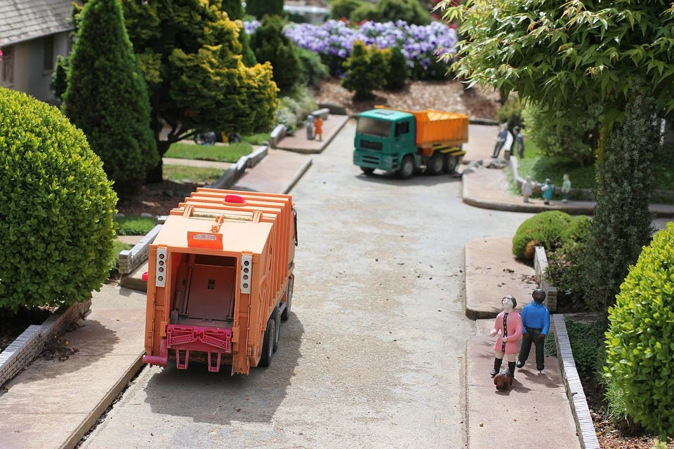 Un modelo en miniatura de una calle con dos camiones de basura de juguete y personas de juguete, simbolizando la recolección de basura.